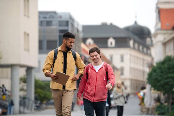 Young man with Down syndrome and his mentoring friend walking and talking outdoors — Stock Photo, Image