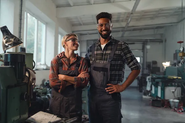 Портрет молодых коллег, работающих в помещении в металлической мастерской, улыбающихся и смотрящих в камеру. — стоковое фото