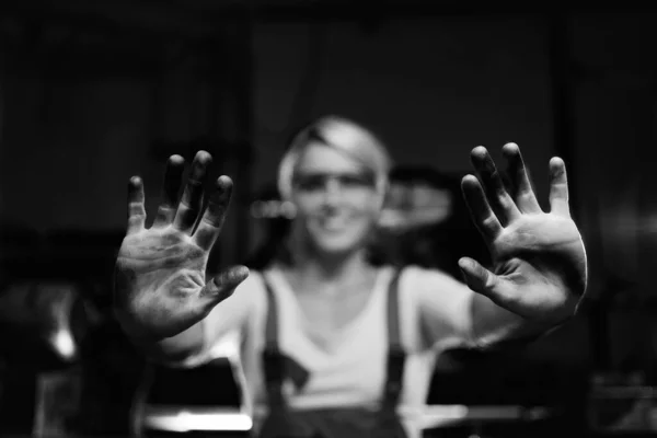 Młoda kobieta pracownik pokazując swoje brudne ręce wewnątrz w warsztacie metalowym — Zdjęcie stockowe