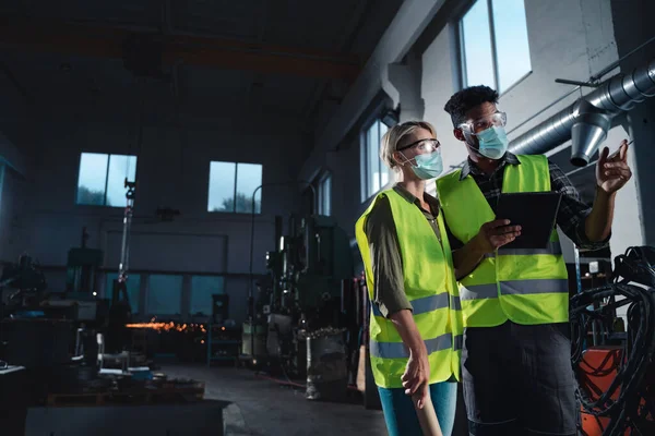 Inspectores industriales con máscaras faciales haciendo un chequeo general en interiores en taller de metal, concepto coronavirus. — Foto de Stock