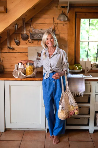 Happy senior woman unpacking shopping indoors at home and looking at camera, sustainable lifestyle. — Stock Photo, Image