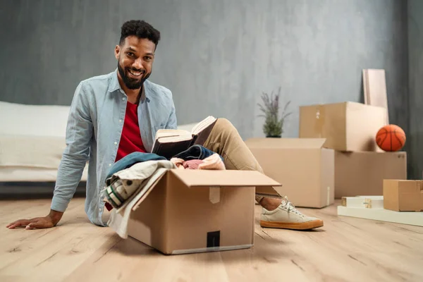 Happy young man putting clothes into packing boxes, moving home. new living concept. — Stock Photo, Image