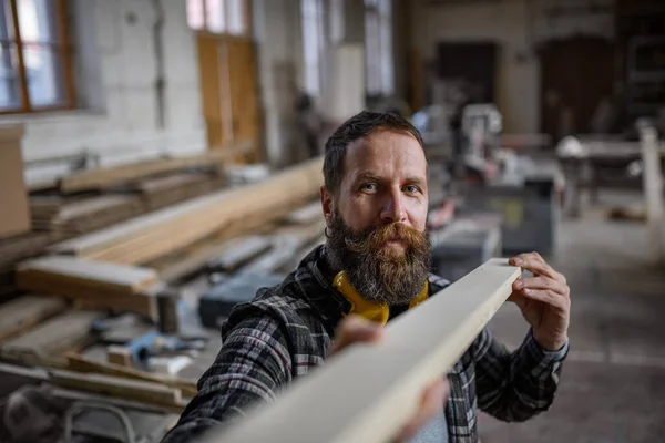 Marangozluk atölyesinde ahşap tahta taşıyan olgun bir erkek marangoz. Küçük işletme kavramı. — Stok fotoğraf