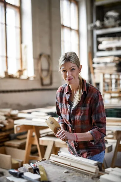 Gözlüklü kadın marangoz ürünü üzerinde çalışıyor, kameraya bakıyor. Küçük işletme kavramı. — Stok fotoğraf