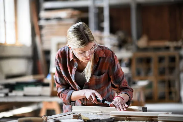 Femme charpentier avec lunettes de travail sur son produit à l'intérieur dans l'atelier de menuiserie. — Photo