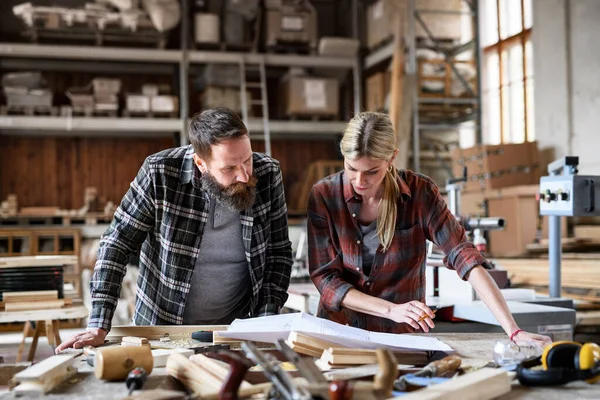 Δύο ξυλουργοί, άντρας και γυναίκα, μιλάνε για σχεδιασμό προϊόντων. Έννοια των μικρών επιχειρήσεων. — Φωτογραφία Αρχείου