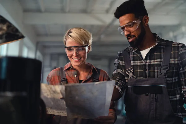 Portrait of young biracial industrial colleagues working indoors in metal workshop, smiling. — Stock Photo, Image