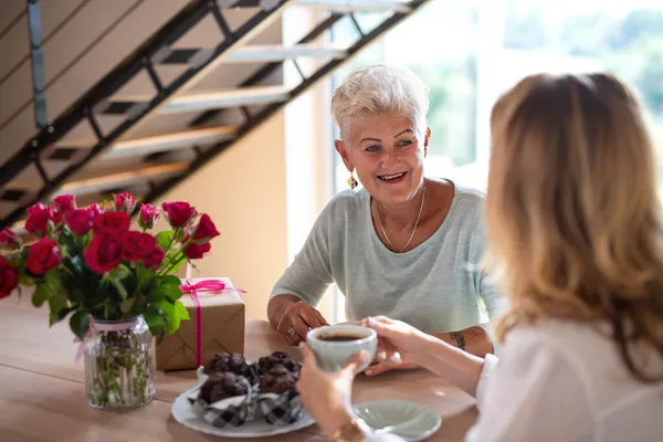 Felice madre anziana che prende un caffè con la figlia adulta al chiuso a casa, seduto e parlando. — Foto Stock