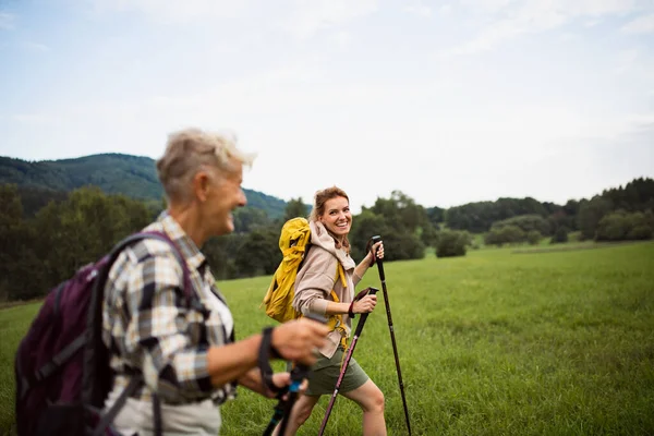 Glad medelvuxen kvinna med vandringsstavar vandring med aktiv senior mor utomhus i naturen. — Stockfoto