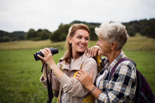Feliz senderista madre mayor abrazándose con hija adulta sosteniendo prismáticos al aire libre en la naturaleza —  Fotos de Stock