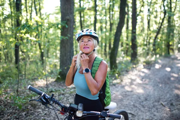 Porträt einer aktiven Seniorin, die sich im Wald einen Helm aufsetzt. — Stockfoto