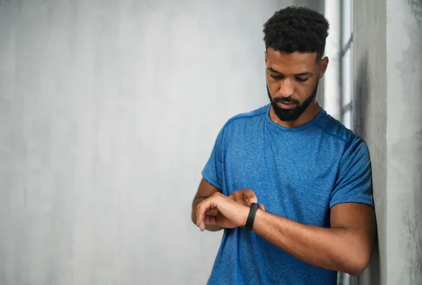 Feliz joven deportista afroamericano de pie en el gimnasio, usando smartwatch, espacio de copia. — Foto de Stock