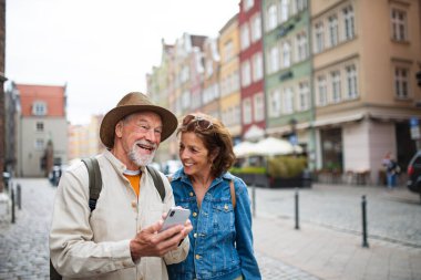 Tarihi şehirde akıllı telefon kullanan mutlu yaşlı çift portresi.