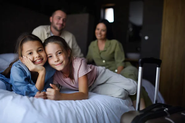 Šťastná mladá rodina se dvěma dětmi sedí na posteli a dívá se na kameru v hotelu, letní dovolená. — Stock fotografie