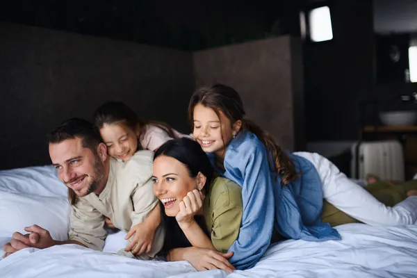 Feliz familia joven con dos niños acostados en la cama en el hotel, vacaciones de verano. — Foto de Stock