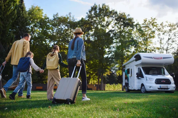 Visão traseira da jovem família com malas indo para caravana ao ar livre no parque. — Fotografia de Stock