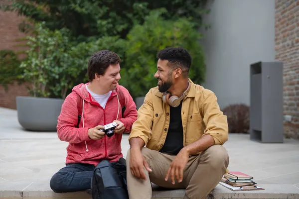 Šťastný mladý muž s Downovým syndromem a mentoring přítel sedí venku — Stock fotografie