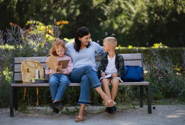 Felice donna anziana con nipoti seduti sulla panchina e aiutare con i compiti all'aperto nel parco. — Foto Stock