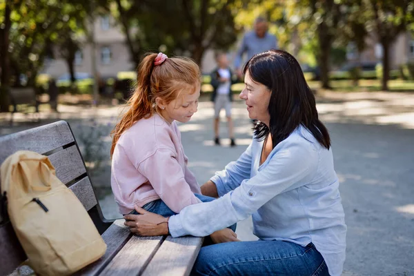 Mujer mayor en cuclillas y hablando con su nieta al aire libre en el banco en el parque. — Foto de Stock