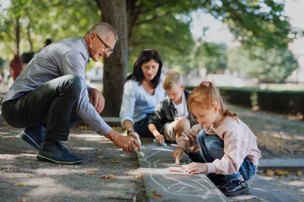 공원에서 길가에 분필을 깐 손 자녀들 과 함께 그림을 그리고 있는 연로 한 부부. — 스톡 사진