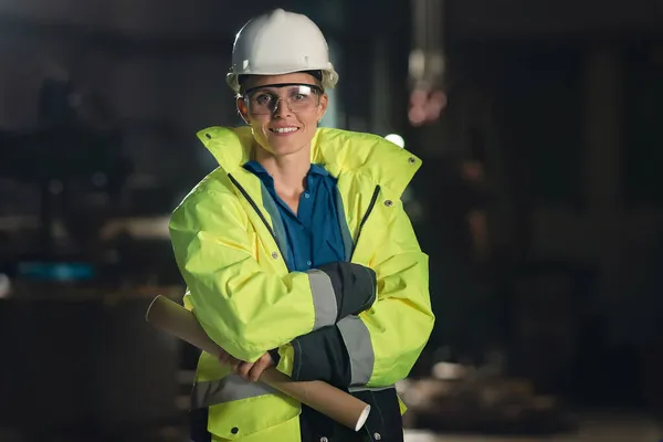 Mujer industrial joven feliz con desgaste protector en interiores en taller de metal, mirando a la cámara. — Foto de Stock