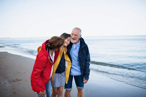 Старша пара та їх онука обіймаються під час прогулянки на піщаному пляжі . — стокове фото