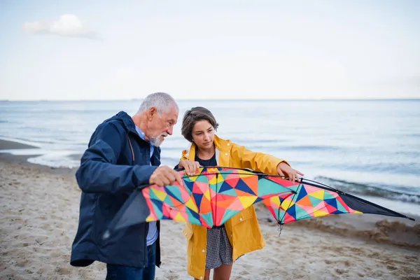 Älterer Mann und seine Enkelin bereiten Drachen für das Fliegen am Sandstrand vor. — Stockfoto