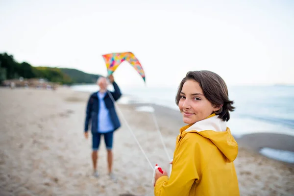 Senior man and his preteen granddaughter playing with kite on sandy beach. — Stock fotografie
