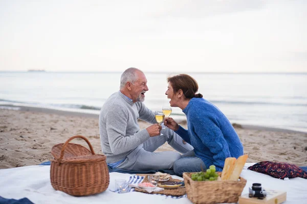 Щаслива старша пара закохана сидячи на ковдрі і маючи пікнік на відкритому повітрі на пляжі біля моря . — стокове фото