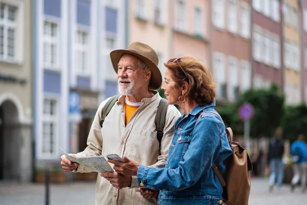 Portret szczęśliwej pary seniorów korzystających z mapy i smartfona na zewnątrz ulicy miasta — Zdjęcie stockowe