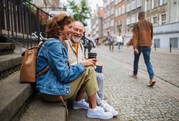 Feliz casal de idosos turistas sentados nas escadas e tendo levado café ao ar livre na cidade — Fotografia de Stock