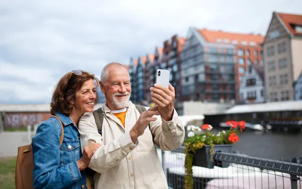 Retrato de feliz casal de idosos turistas fazendo selfie ao ar livre na cidade histórica — Fotografia de Stock