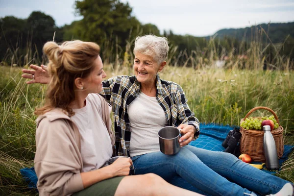 Happy senior mother and adult daughter sitting and having picnic outdoors in nature, talking. — Stock Photo, Image