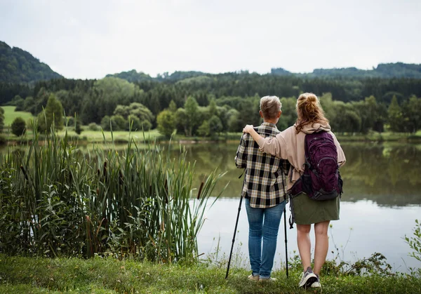 Rear view of senior mother embracing with adult daughter when standing by lake outdoors in nature — Stock Photo, Image