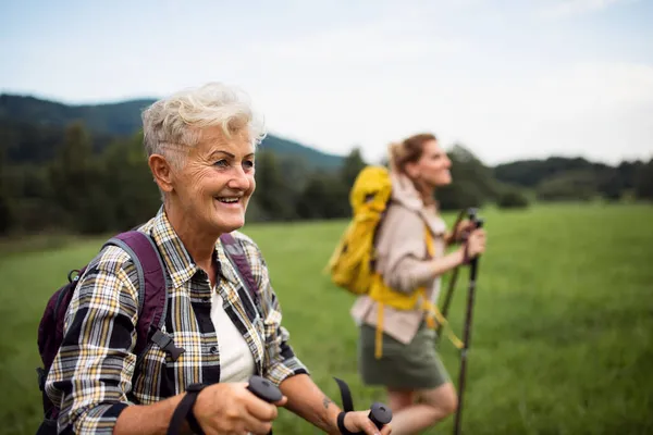 Happy mid adult woman with trekking poles hiking with active senior mother outdoors in nature. — Stock Photo, Image