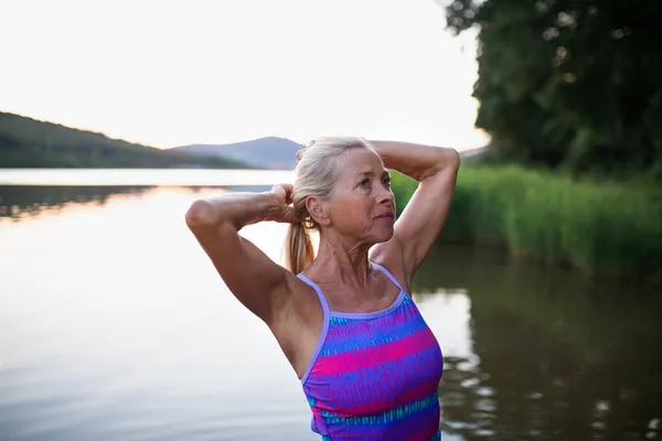 Retrato de mujer mayor activa nadadora de pie y estirándose al aire libre en el lago. — Foto de Stock