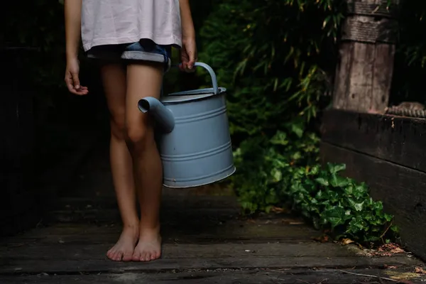 Låg del av liten flicka i shorts håller vattenkanna utomhus i trädgården. — Stockfoto