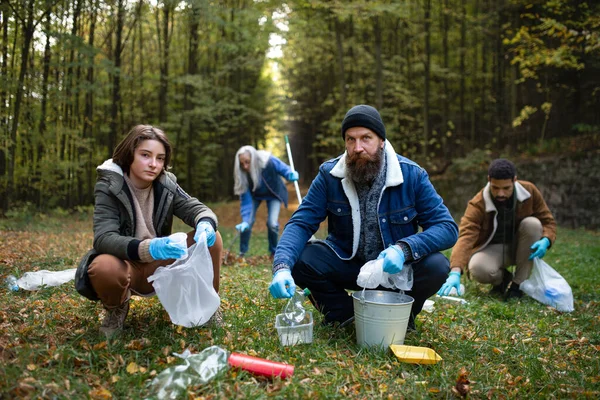 Gruppo di volontari che guardano alla telecamera e ripuliscono la foresta dai rifiuti, concetto di servizio alla comunità — Foto Stock