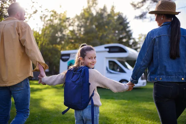 Vista trasera de la niña mirando a la cámara y sosteniendo a los padres cuando van a la caravana al aire libre en el parque. —  Fotos de Stock