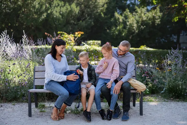 Senior couple with grandchildren sitting on bench, eating snack and talking outdoors in park. — Stock Photo, Image