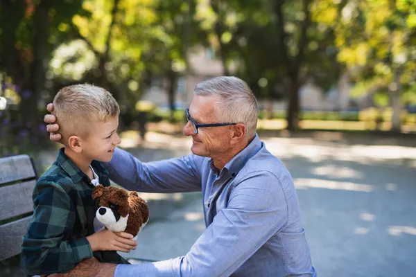 Hombre mayor en cuclillas y hablando con su nieto al aire libre en el banco en el parque. — Foto de Stock