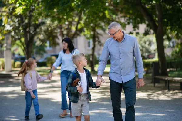 Šťastní prarodiče vzít vnoučata domů ze školy, procházky venku na ulici. — Stock fotografie