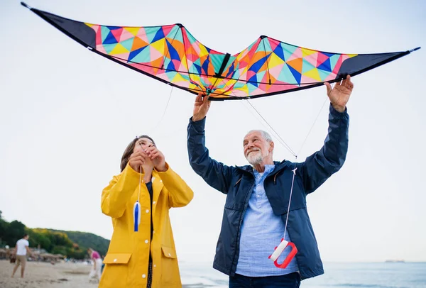 Lage hoek uitzicht op een mooi meisje en haar grootvader spelen met vlieger op zandstrand. — Stockfoto