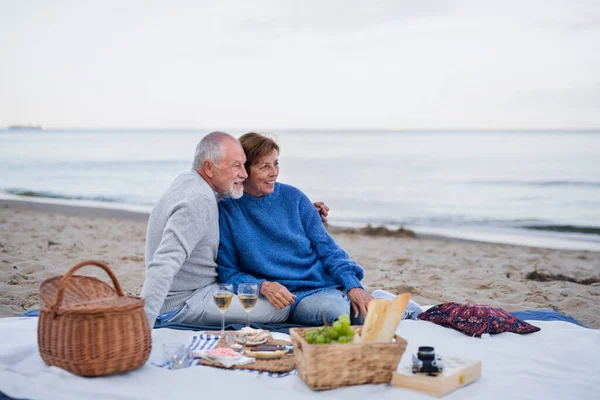 Feliz casal sênior no amor sentado no cobertor e ter piquenique ao ar livre na praia por mar. — Fotografia de Stock