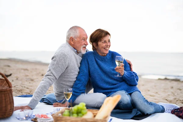 Щаслива старша пара закохана, сидячи на ковдрі і обіймаючись, коли пікнік на відкритому повітрі на пляжі — стокове фото