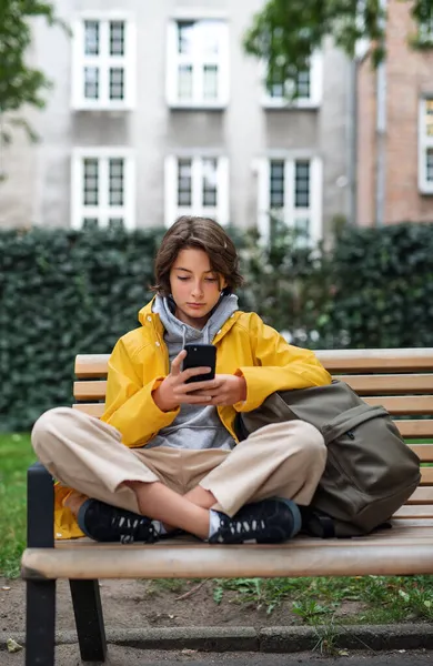 П'ятнадцять школярка сидить на лавці і використовує смартфон на відкритому повітрі в місті . — стокове фото