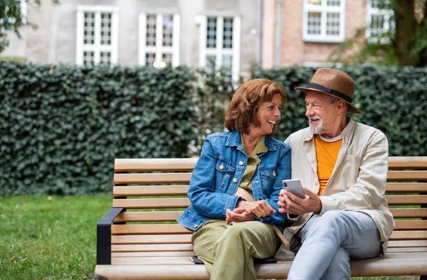 Ευτυχισμένο ζευγάρι ηλικιωμένων στην αγάπη κάθεται στον πάγκο και τη χρήση smartphone σε εξωτερικούς χώρους στην πόλη, αντιγραφή χώρου. — Φωτογραφία Αρχείου