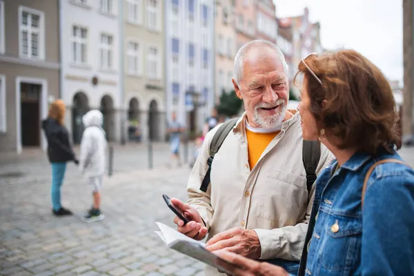 Портрет счастливой пожилой пары туристов с помощью карты и смартфона на улице города — стоковое фото