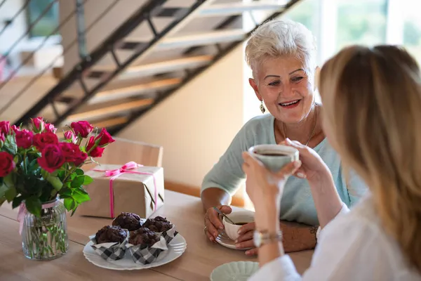 Счастливая пожилая мать пьет кофе со взрослой дочерью дома, сидит и разговаривает. — стоковое фото
