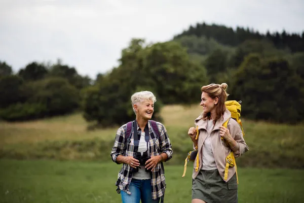 Active senior woman with binoculars hiking with her adult daughter outdoors in nature. — Stock Photo, Image